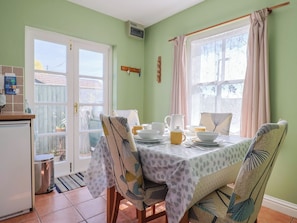Un comedor con una mesa dispuesta para cuatro personas, sillas con tapicería estampada, una ventana con cortinas y vistas al exterior.