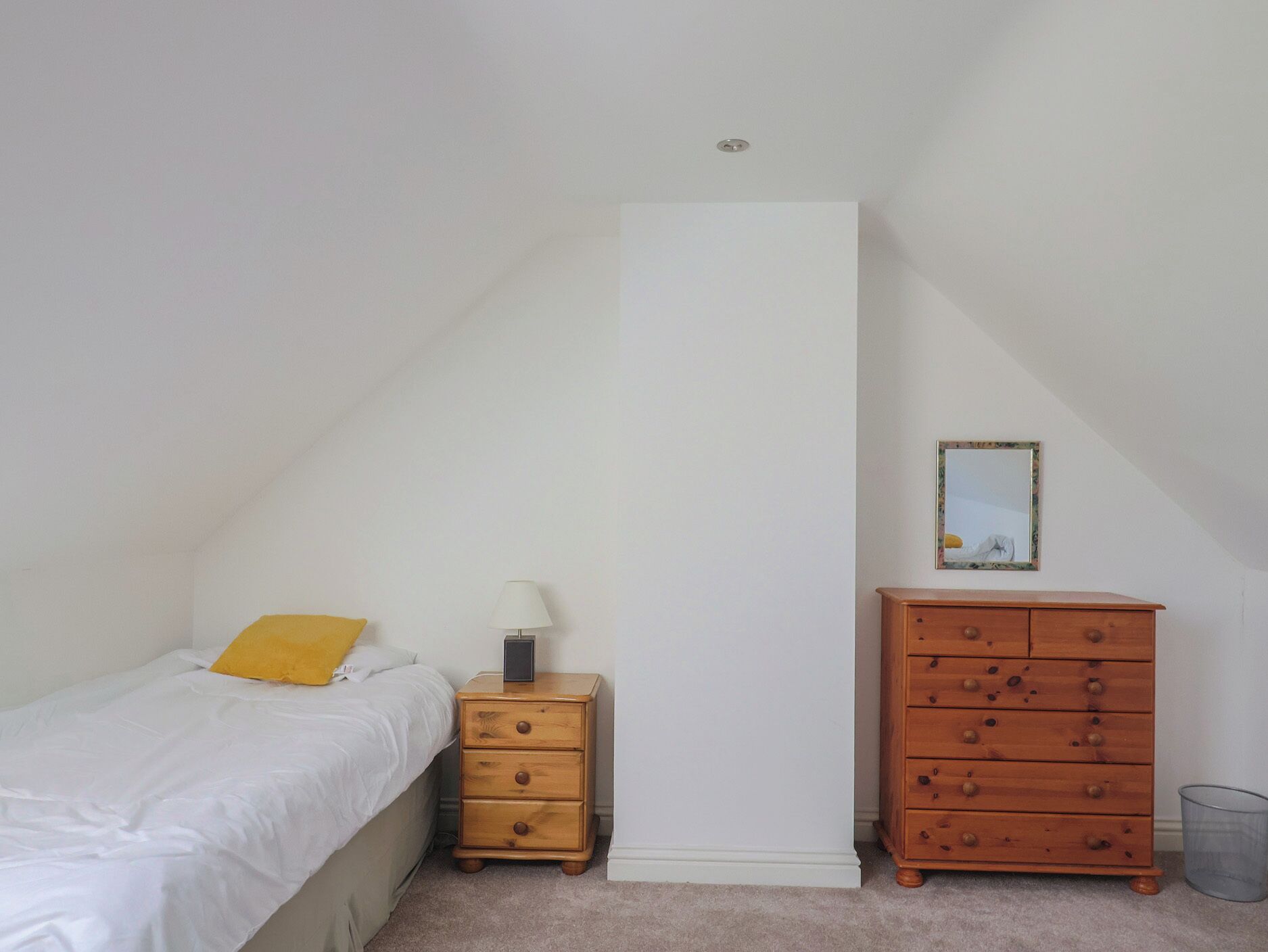 Een slaapkamer met een bed, nachtkastje met een lamp, een houten dressoir en een lijst met een foto aan de muur.