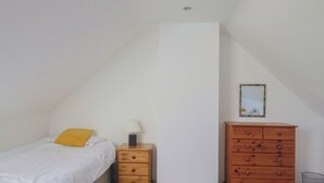 A bedroom with a bed, a nightstand with a lamp, a wooden dresser, and a framed picture on the wall. - Morpeth (Chard)