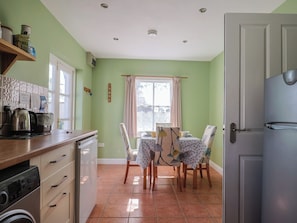 Una cocina con lavadora, cafetera y comedor con mesa y sillas.