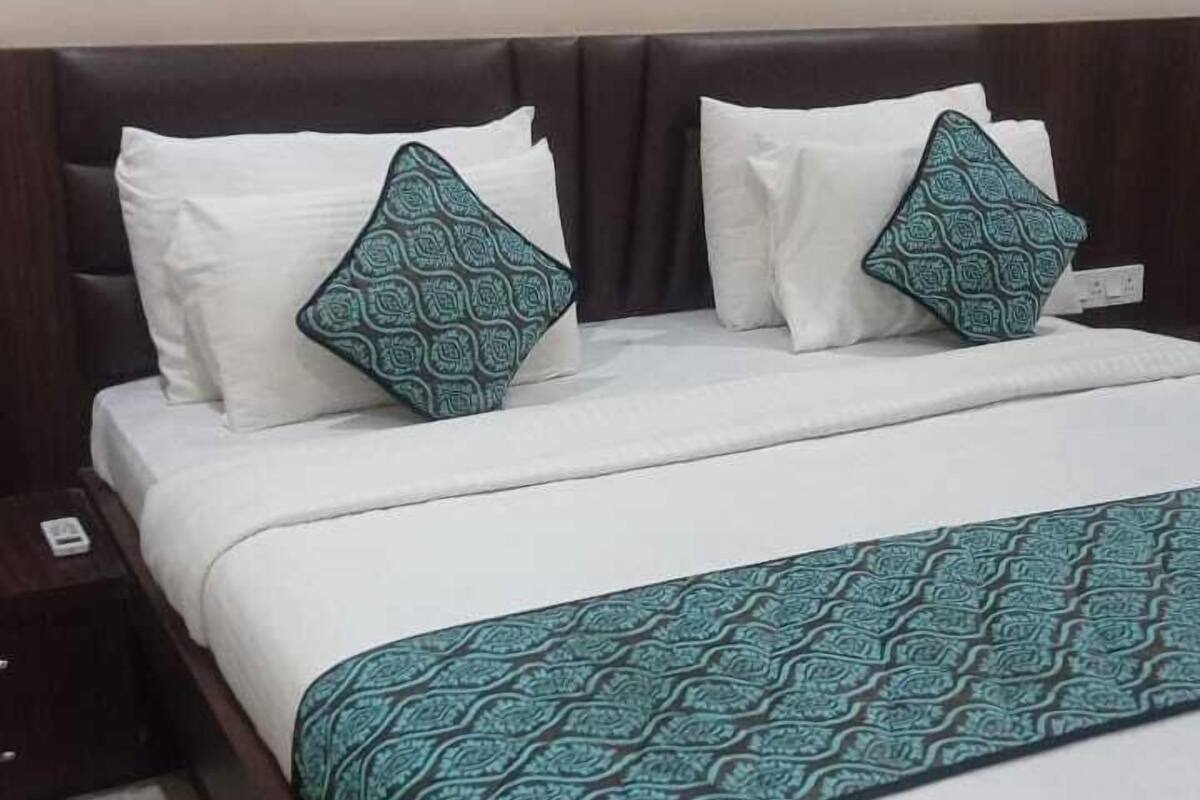 A neatly made bed with white and teal bedding, a dark headboard, and a patterned throw.