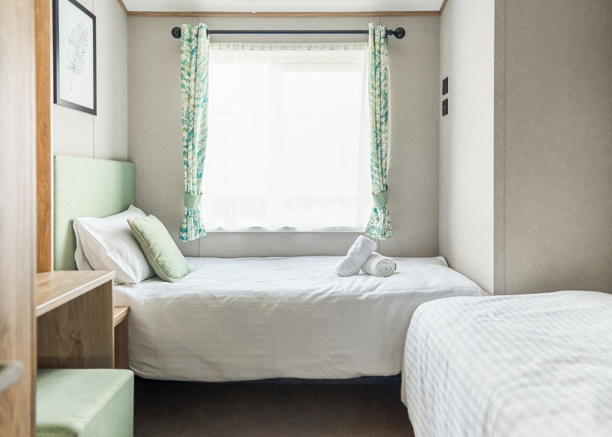 A small, neatly arranged bedroom with a single bed, a bedside table, and a window with curtains.