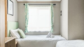 A small, neatly arranged bedroom with a single bed, a bedside table, and a window with curtains.