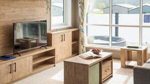 A modern living room with a TV, wooden cabinets, a small table with a book, and a bowl of fruit.