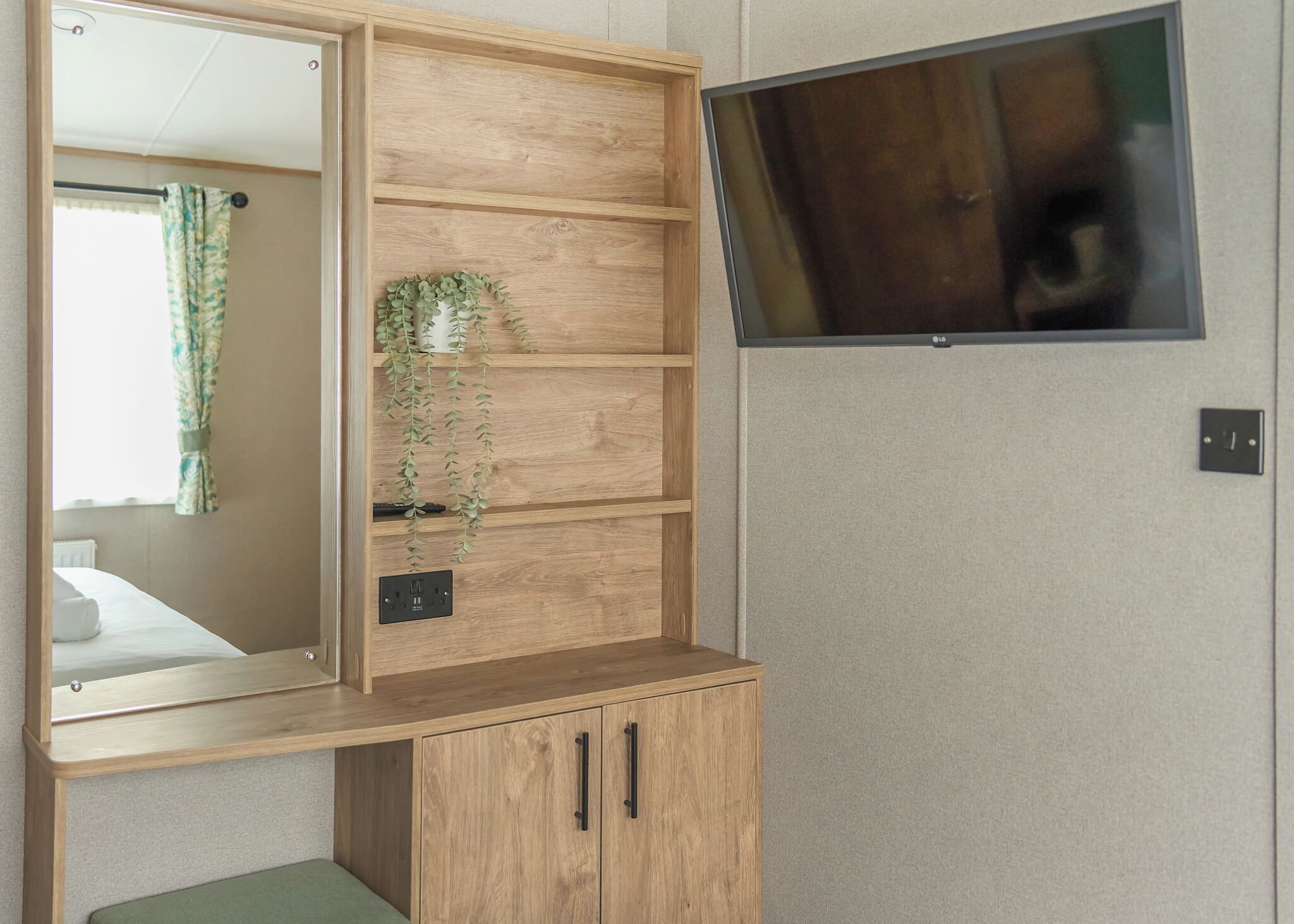 Ein Holzkabinett mit Spiegel, ein an der Wand montierter Fernseher und eine Steckdose.