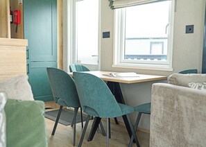A compact room with a dining table, teal chairs, a sofa, and a window with a view. - Premium 3 bed HT Pet (Landford, Nr Salisbury)