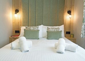 A neatly made bed with pillows, a book, and towels on a wooden nightstand. - Premium 3 bed HT Pet (Landford, Nr Salisbury)