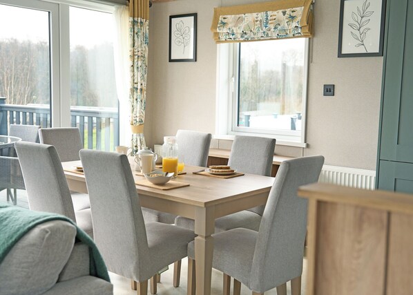 A dining area with a table set for breakfast, chairs, a window with curtains, and framed artwork on the wall.