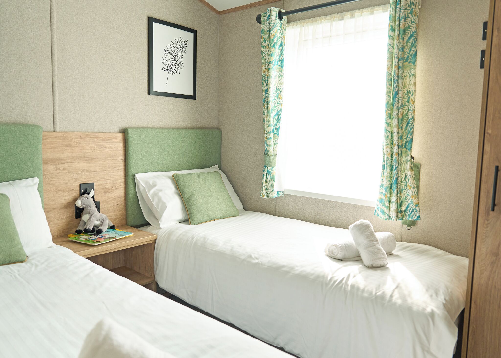 A bedroom with two beds, a nightstand with a lamp, a framed picture on the wall, and a window with curtains.