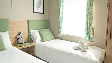 A bedroom with two beds, a nightstand with a lamp, a framed picture on the wall, and a window with curtains.