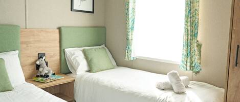 A bedroom with two beds, a nightstand with a lamp, a framed picture on the wall, and a window with curtains.