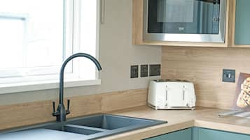 A kitchen with a double sink, a microwave, a toaster, and wooden cabinetry.