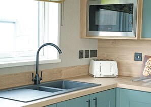 A kitchen with a double sink, a microwave, a toaster, and wooden cabinetry. - Exclusive Lodge 4 bed HT (Landford, Nr Salisbury)