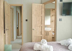 A hotel room with wooden doors, a bed with a rolled towel, a sink, and a TV mounted on the wall.