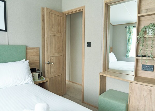 A bedroom with a bed, a wooden wardrobe, a mirror, and a small bedside table with a cup and a book.