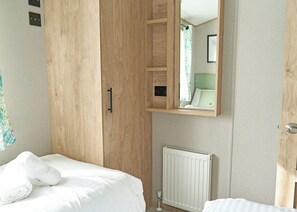 A bedroom with a wooden wardrobe, a bed with white bedding, a radiator, and a mirror reflecting a bathroom.