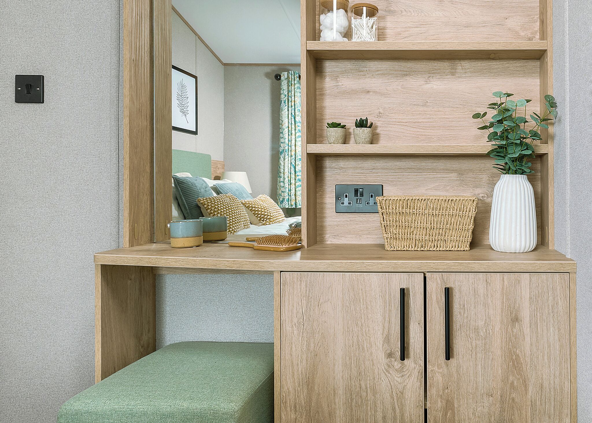 A room with a wooden desk, a mirror, a green bench, and a shelf with decorative items.