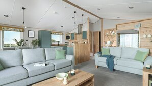 Un salon moderne avec deux canapés gris, une table basse en bois et un coin cuisine doté de meubles en bois et d’une fenêtre.