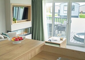 A modern living room with a flat-screen TV, a fireplace, a dining area with a table and chairs, and a sliding glass door leading to an outdoor patio with a hot tub. - 3 bedroom accommodation in Landford, Nr Salisbury (Landford, Nr Salisbury)
