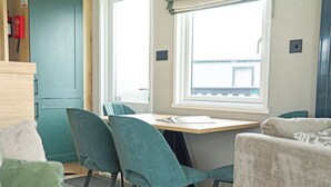 A compact room with a wooden table, teal chairs, a window with a view, and a kitchenette area. - 3 bedroom accommodation in Landford, Nr Salisbury (Landford, Nr Salisbury)