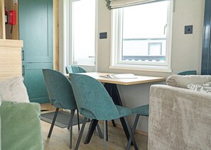 A compact room with a wooden table, teal chairs, a window with a view, and a kitchenette area. - 3 bedroom accommodation in Landford, Nr Salisbury (Landford, Nr Salisbury)
