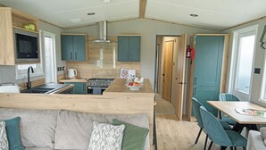 A compact kitchen with a stove, sink, and microwave. There is a dining area with a table and chairs. - 3 bedroom accommodation in Landford, Nr Salisbury (Landford, Nr Salisbury)