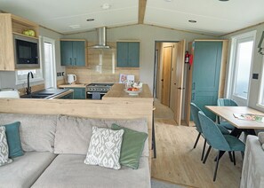 A compact kitchen with a stove, sink, and microwave. There is a dining area with a table and chairs. - 3 bedroom accommodation in Landford, Nr Salisbury (Landford, Nr Salisbury)