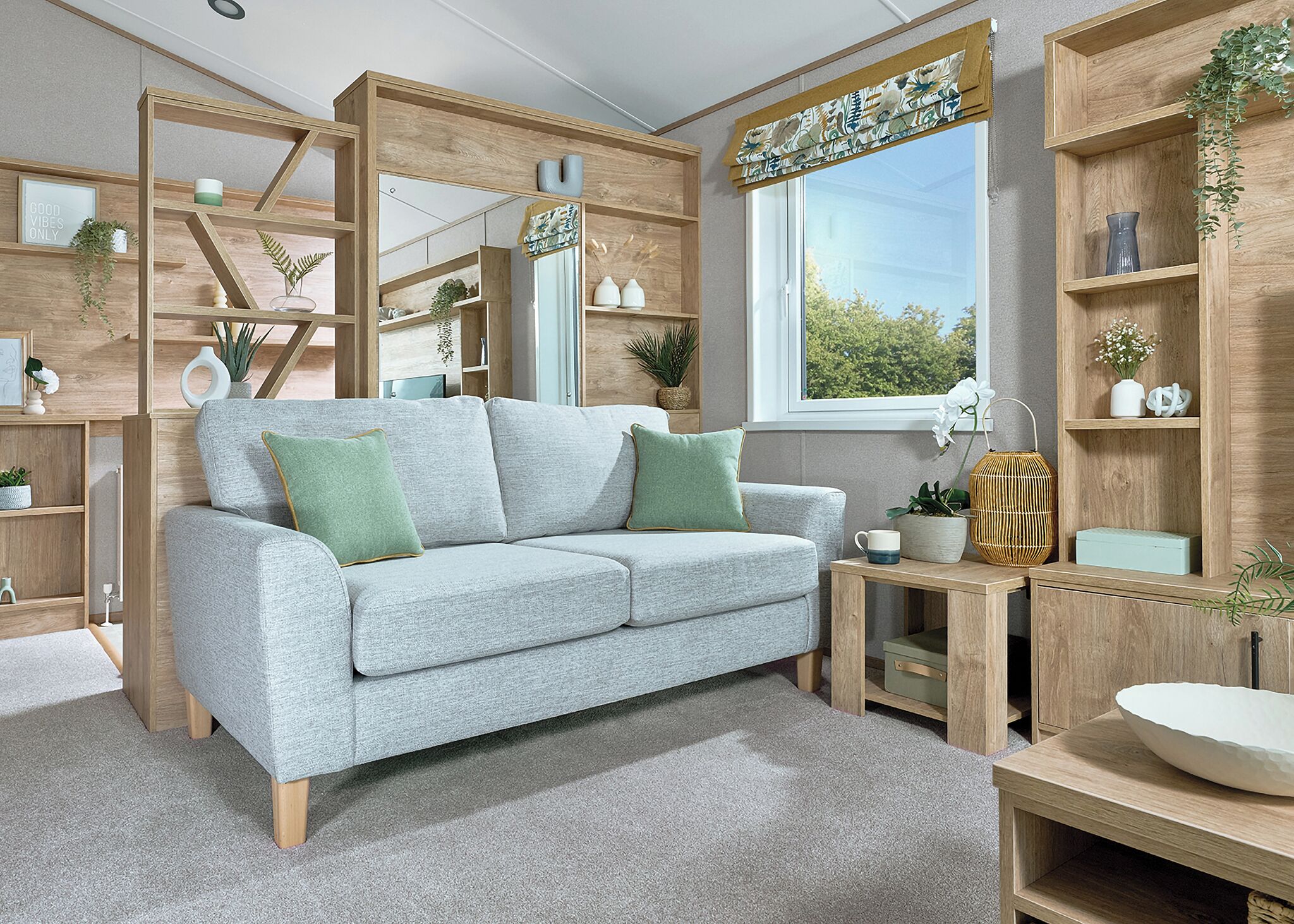 Un salon moderne avec un canapé gris, des étagères en bois et une fenêtre donnant sur un paysage agréable.