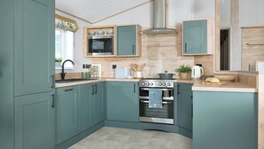 A kitchen with teal cabinets, a stainless steel range hood, a built-in oven, and a microwave. - Exclusive Lodge 3 bed HT (Great Yarmouth)
