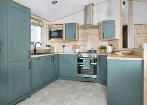 A kitchen with teal cabinets, a stainless steel range hood, a built-in oven, and a microwave. - Exclusive Lodge 3 bed HT (Great Yarmouth)