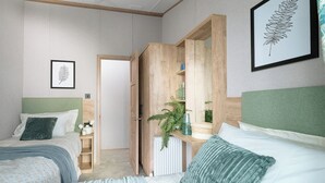 A bedroom with two beds, a wooden wardrobe, a radiator, and a framed plant on the wall. - Exclusive Lodge 3 bed HT (Great Yarmouth)