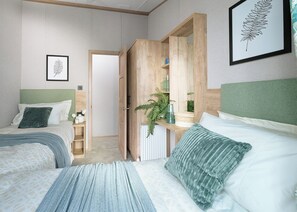 A bedroom with two beds, a wooden wardrobe, a radiator, and a framed plant on the wall. - Exclusive Lodge 3 bed HT (Great Yarmouth)