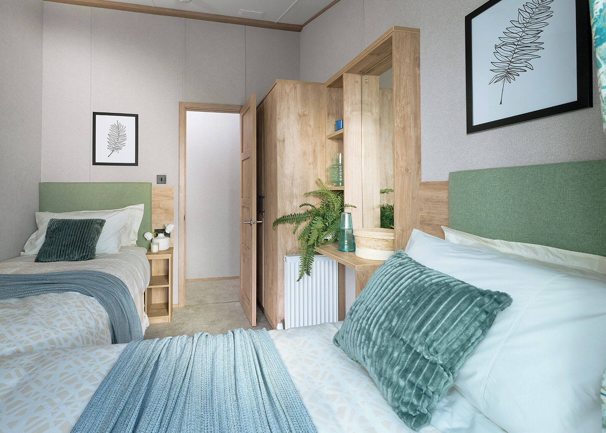 A bedroom with two beds, a wooden wardrobe, a radiator, and a framed leaf artwork.