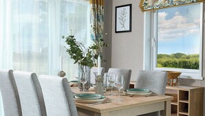 Een eettafel met stoelen, een vaas met planten, wijnglazen en een fotokader aan de muur.