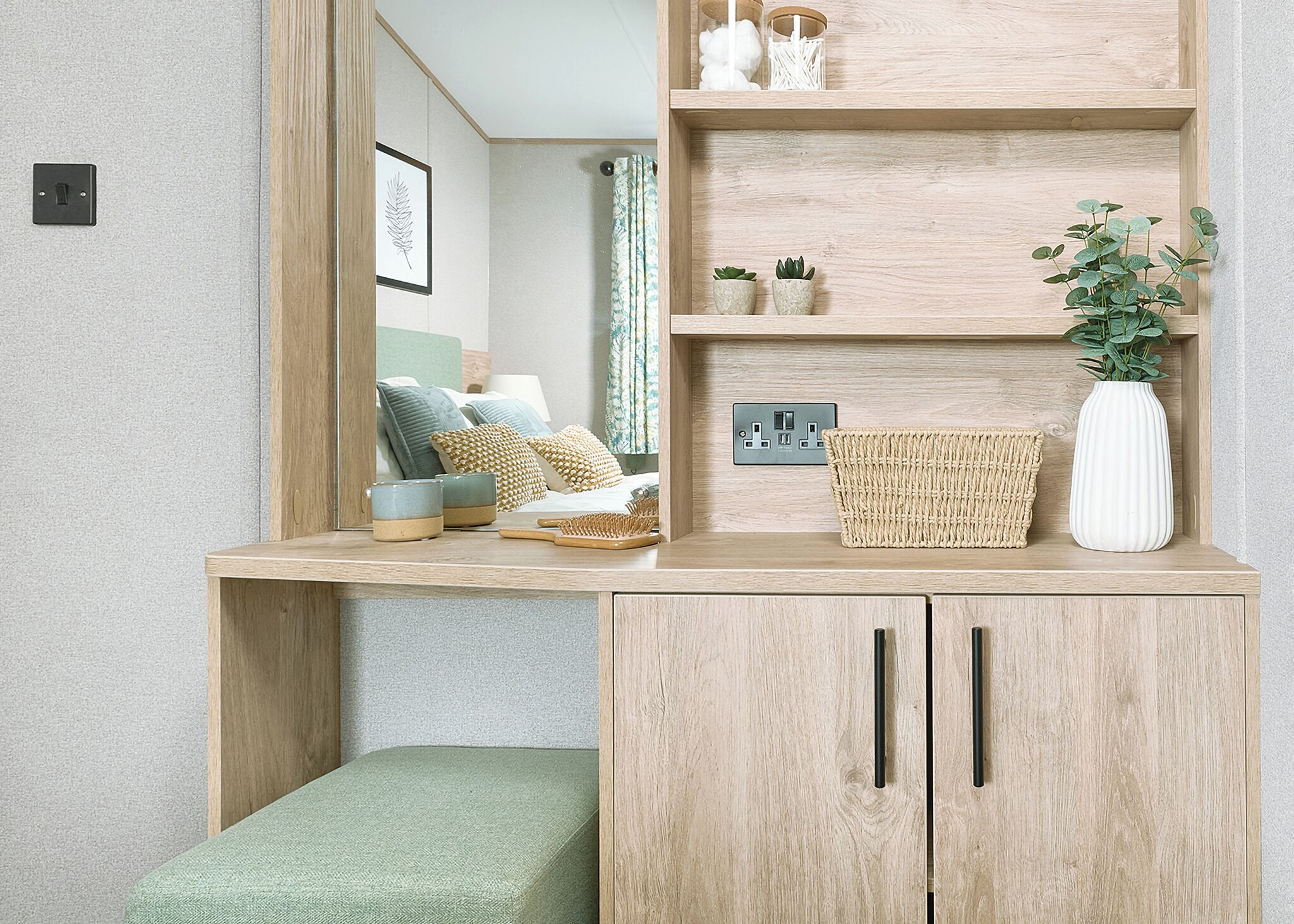 A room with a bed, a wooden desk, a mirror, and a shelf with decorative items.