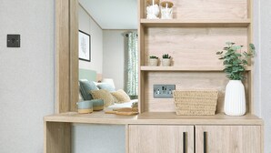 Een kamer met een bed, een houten bureau, een spiegel en een plank met decoratieve objecten.