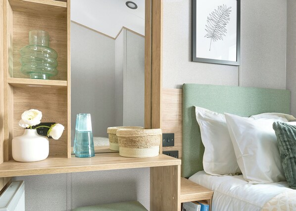 A bedroom with a bed, a bedside table with a vase, a blue bottle, and a framed leaf artwork.