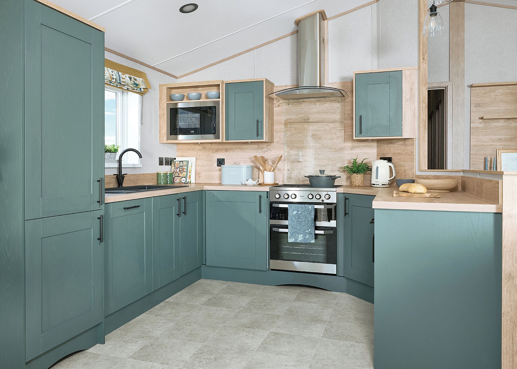 Une cuisine avec des meubles de couleur bleu-vert, un four encastré, un four à micro-ondes et une cuisinière.