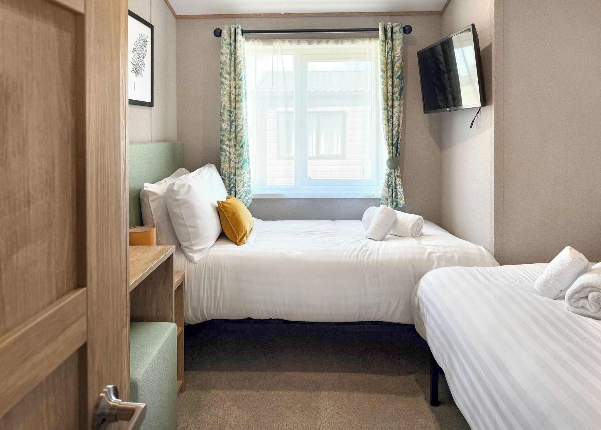 A hotel room with a bed, a TV mounted on the wall, and a window with curtains.