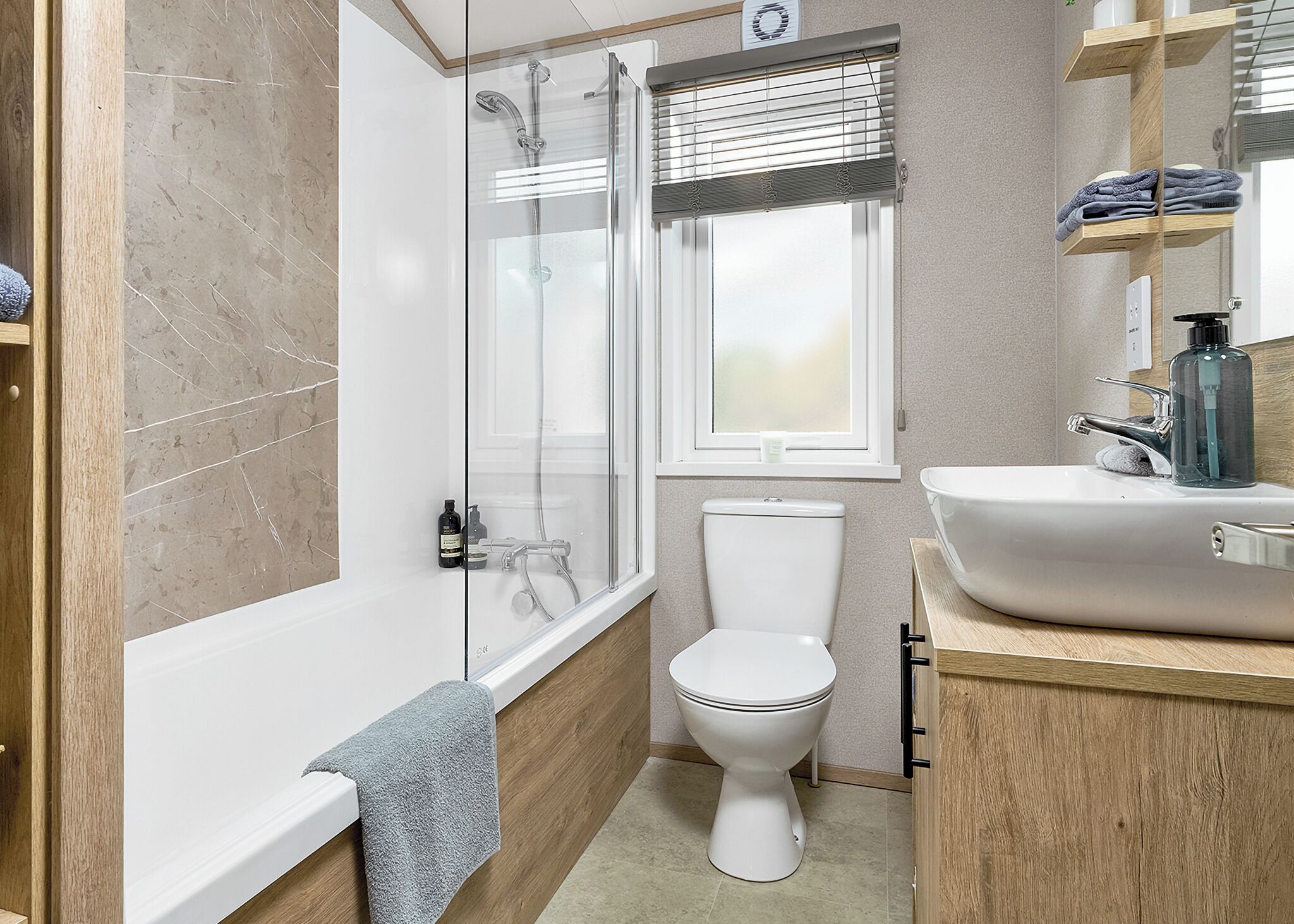 Une salle de bain avec une douche à parois de verre, des toilettes, un lavabo et une fenêtre avec des stores.