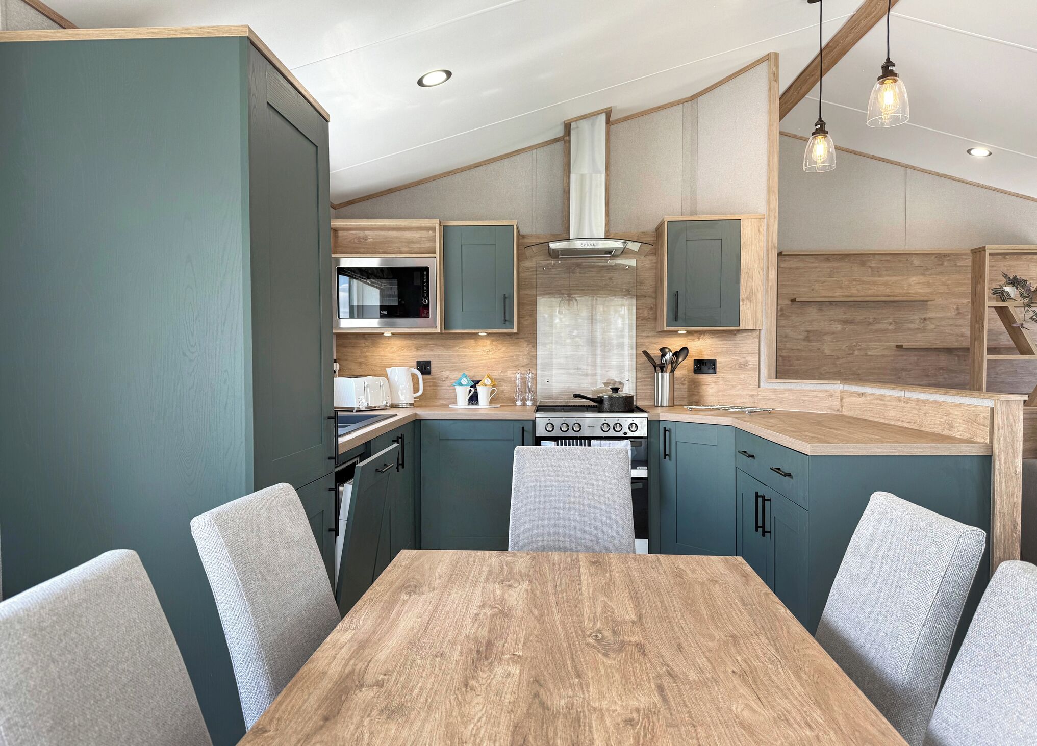 A modern kitchen with a wooden table and chairs, built-in appliances, and pendant lighting.