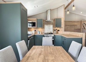 A modern kitchen with a wooden table and chairs, built-in appliances, and pendant lighting. - Exclusive Lodge 4 bed HT (Great Yarmouth)