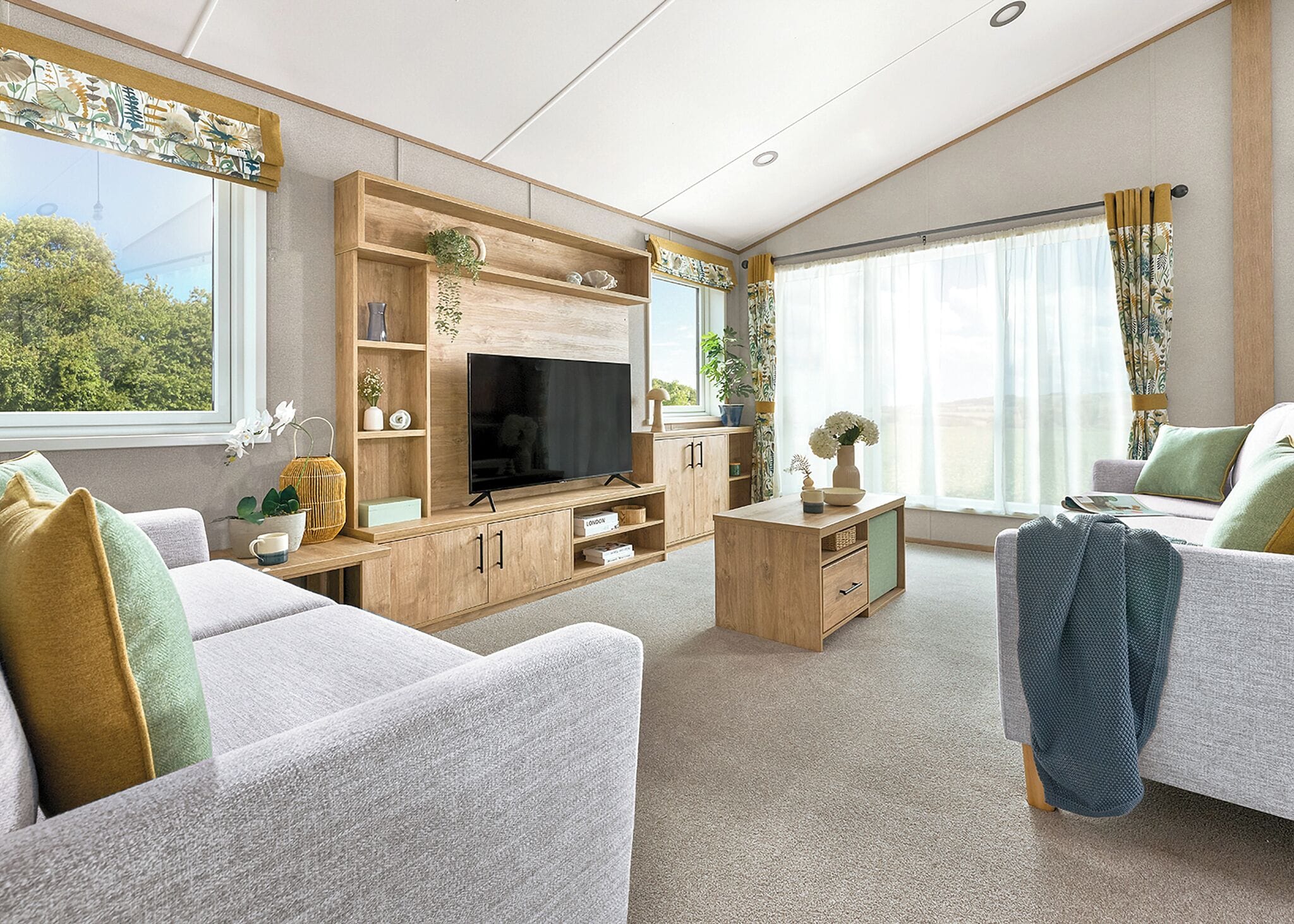 A modern living room with a flat-screen TV, wooden furniture, and large windows.
