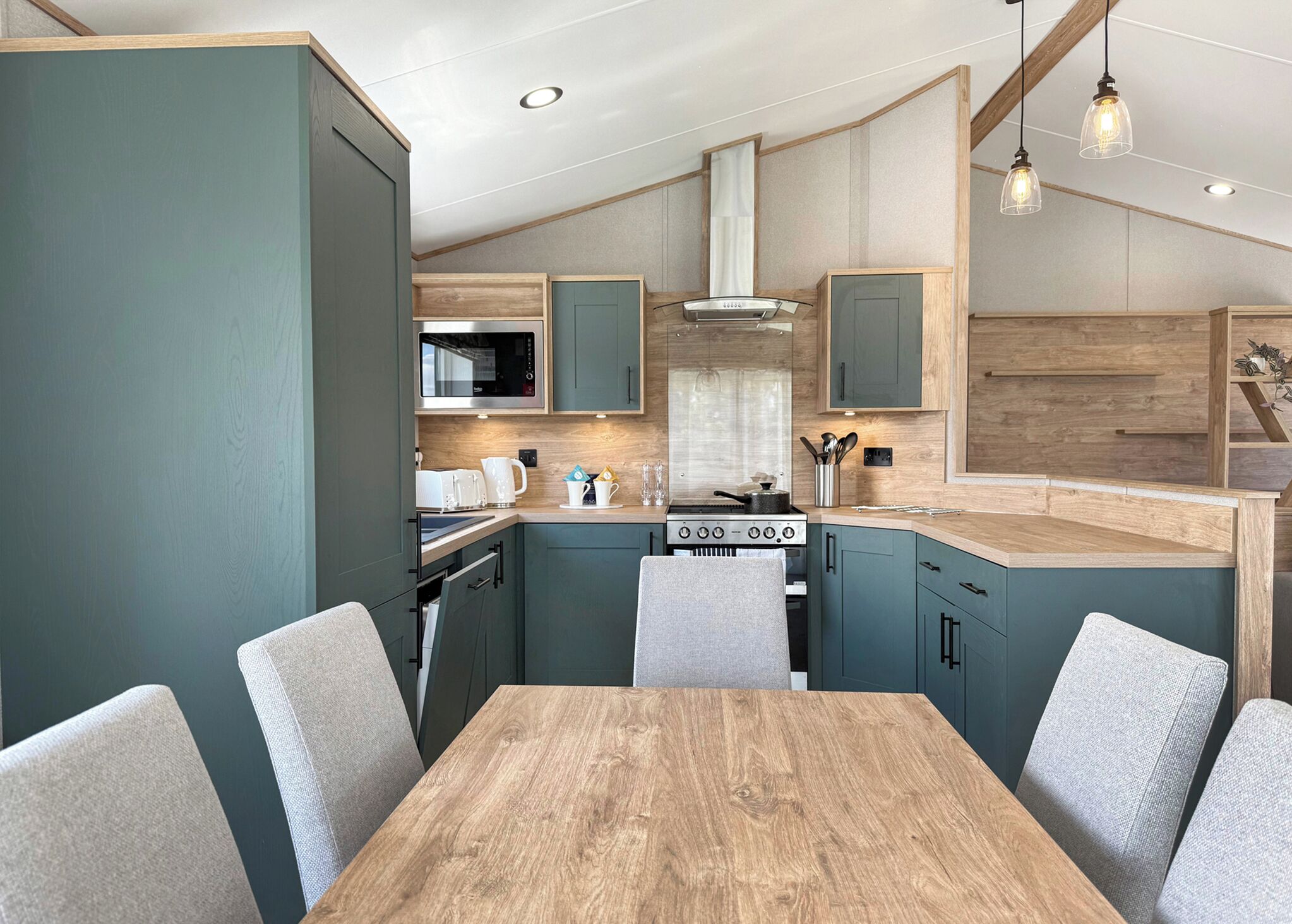 A modern kitchen with teal cabinetry, a wooden dining table, and pendant lighting.