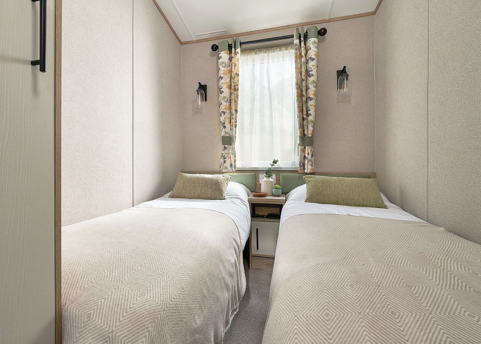 Une chambre avec deux lits, une petite table sur laquelle est posée une plante, une fenêtre avec des rideaux et un luminaire fixé au mur.