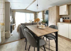A modern kitchen with a wooden dining table, grey chairs, and a hanging light fixture. - 2 bedroom accommodation in Great Yarmouth (Great Yarmouth)