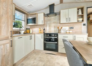 A modern kitchen with white cabinets, a built-in oven, a microwave, and a dining area with a table and chairs. - 2 bedroom accommodation in Great Yarmouth (Great Yarmouth)