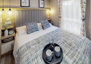 A neatly made bed with a striped blanket, two pillows, bedside tables with lamps, a tray with two mugs, and framed artwork on the wall. - 2 bedroom accommodation in Great Yarmouth (Great Yarmouth)