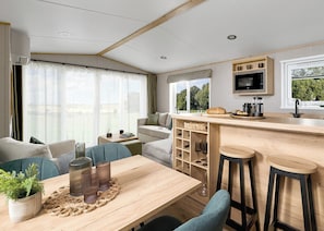 Ein modernes Wohnmobil-Interieur mit Essbereich, Barhocker, einer Küche inklusive Mikrowelle und einem großen Fenster mit Aussicht.
