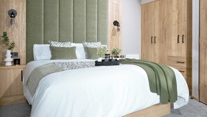 A bedroom with a large bed, wooden wardrobe, and a green upholstered headboard. - Premium Holiday Home 3 bed HT Pet (Great Yarmouth)